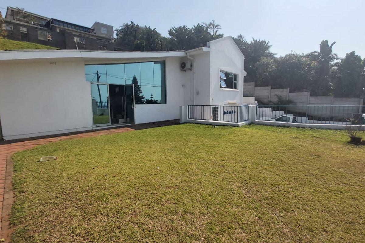 Rear view of the property featuring a large lawn, paved walkway, and a modern reflective glass facade with sliding door access.