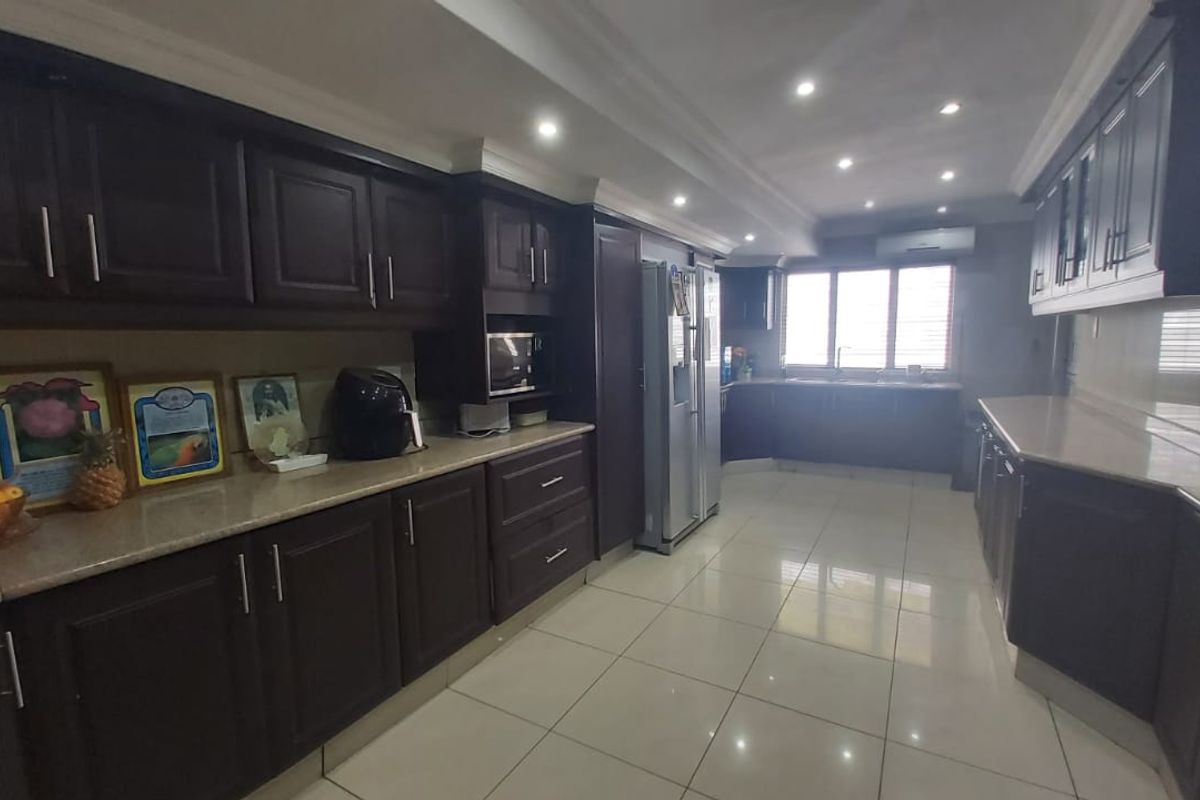 Spacious kitchen featuring dark wood cabinetry, stone countertops, tiled flooring, and integrated appliances with recessed lighting.
