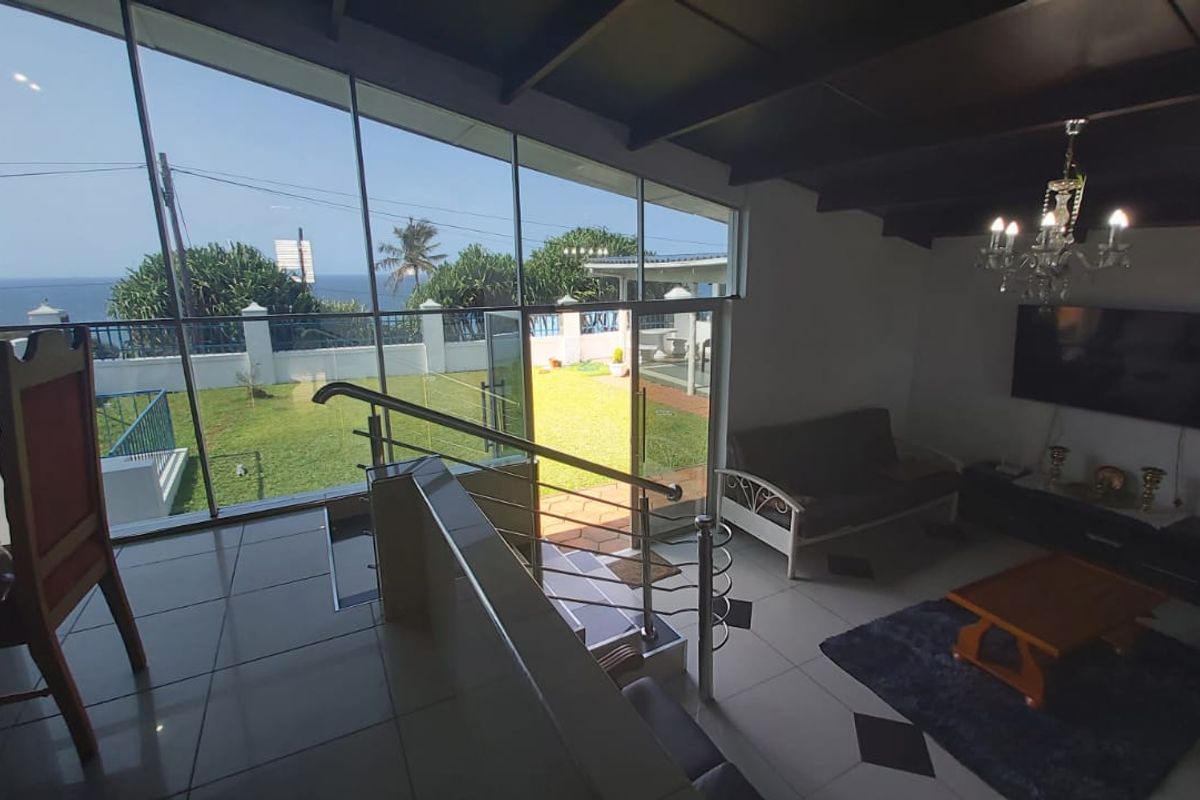 Spacious living area featuring floor-to-ceiling windows with ocean views, exposed timber ceiling beams, and modern tiled flooring with decorative accents.