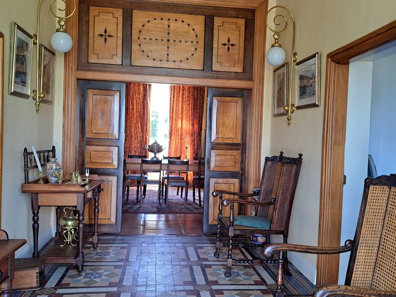 A grand hallway featuring intricate decorative floor tiling, classic wooden door frames, and elegant wall-mounted brass lighting fixtures leading into the dining area.
