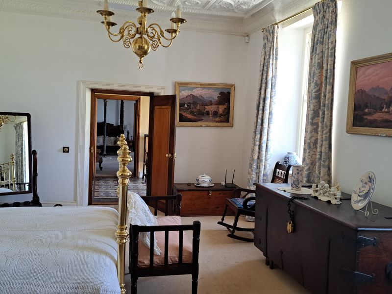 Spacious bedroom featuring classic architectural details, including ornate ceiling molding, a brass chandelier, and traditional timber door frames.
