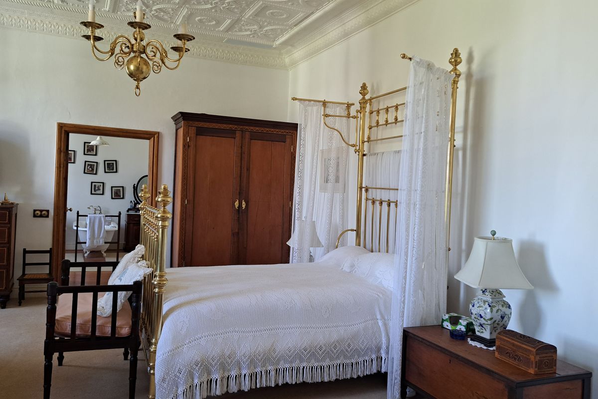 Spacious bedroom featuring an ornate plaster ceiling, crown molding, and a classic brass chandelier, with an adjoining view into a bathroom.