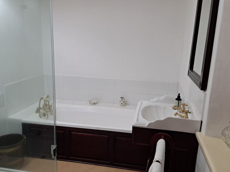 A well-maintained bathroom featuring a bathtub, a separate glass-enclosed shower, and a classic pedestal sink with brass fixtures.