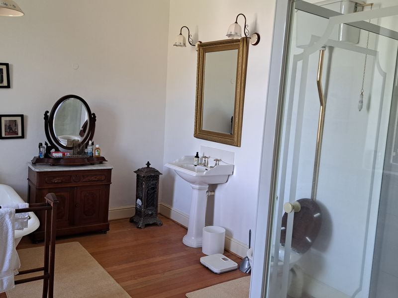 A spacious bathroom featuring a classic clawfoot bathtub, a pedestal basin, and a separate shower enclosure with hardwood flooring.
