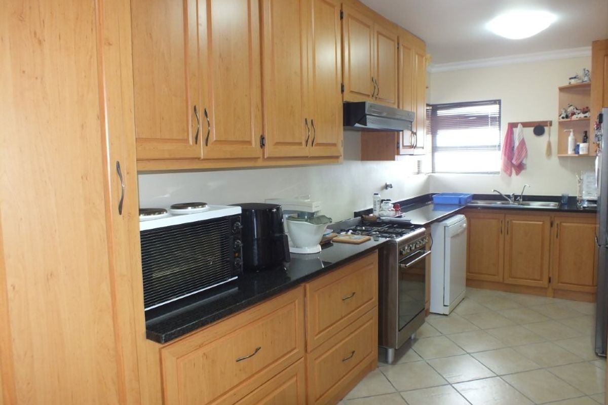 A functional kitchen featuring wooden cabinetry, dark granite countertops, a gas stove with extractor fan, and tiled flooring.