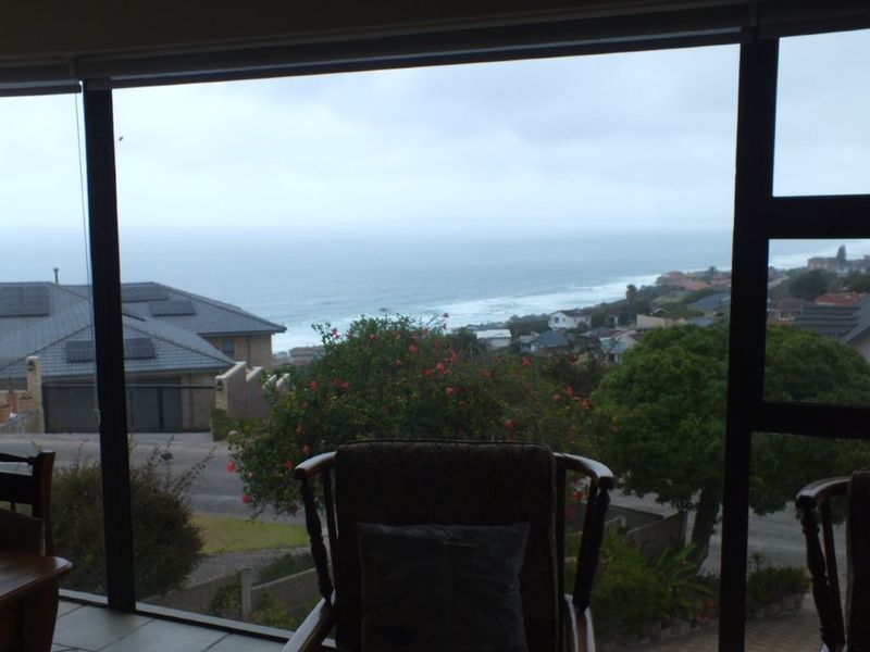A view from inside looking out through large windows, showcasing a coastal landscape and residential neighbourhood.
