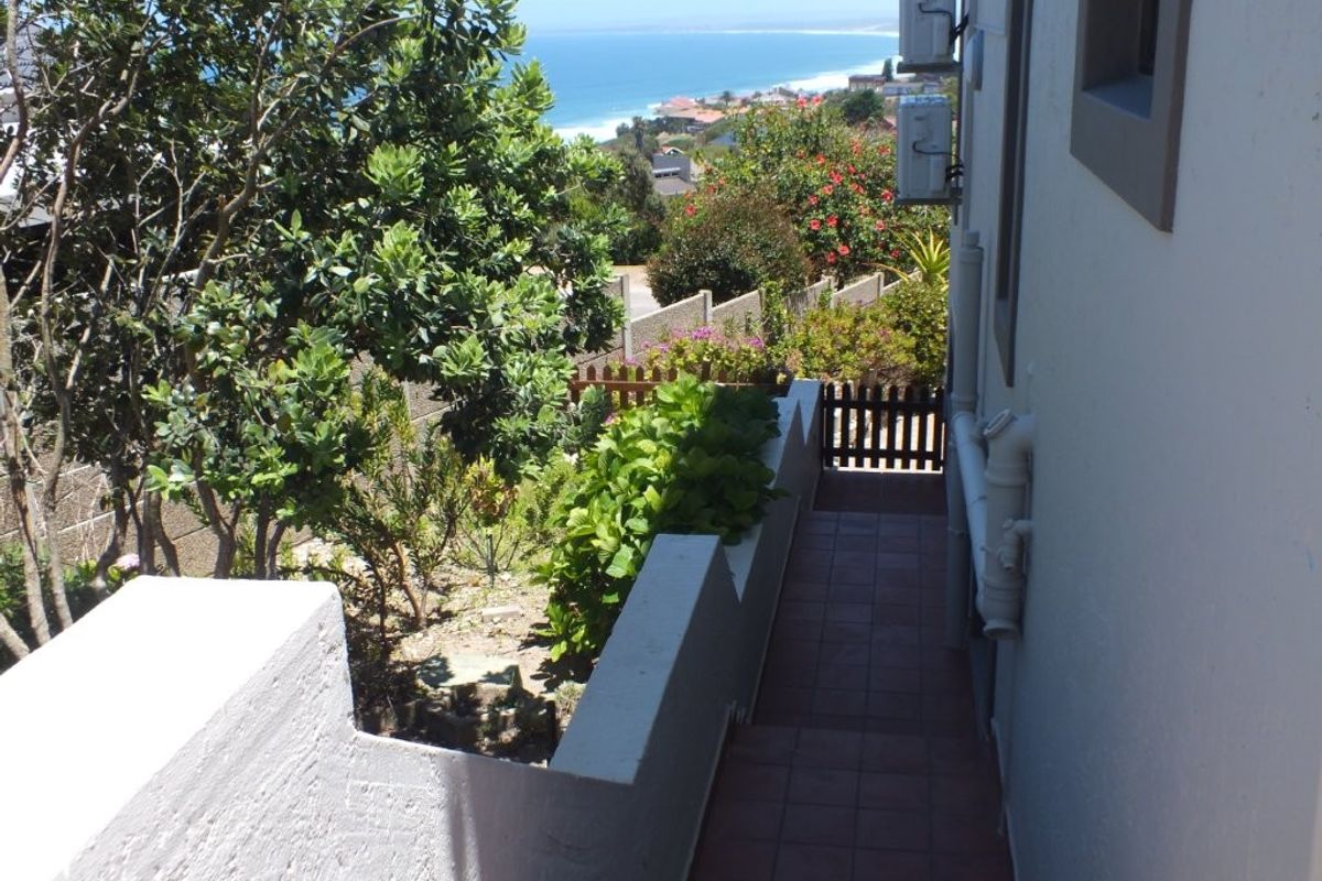 A side pathway with tiled flooring leading towards a garden area, featuring coastal views and mounted air conditioning units on the exterior wall.