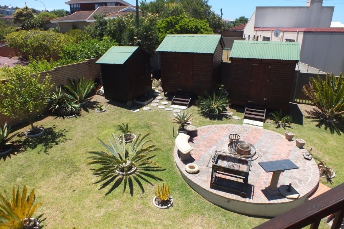 A spacious rear garden featuring a circular paved patio area, multiple wooden storage sheds, and established landscaping.