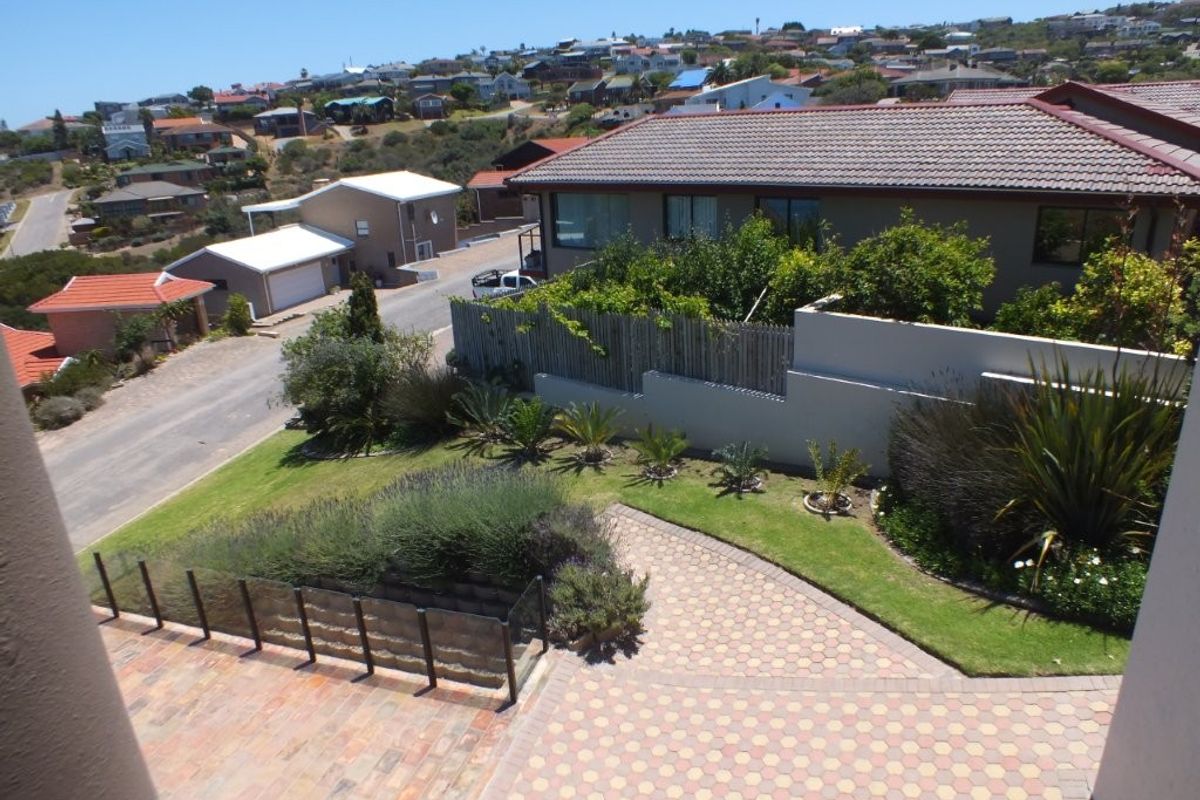 Elevated view overlooking a landscaped garden with paved driveway, retaining walls, and glass balustrading, set within a residential neighbourhood.