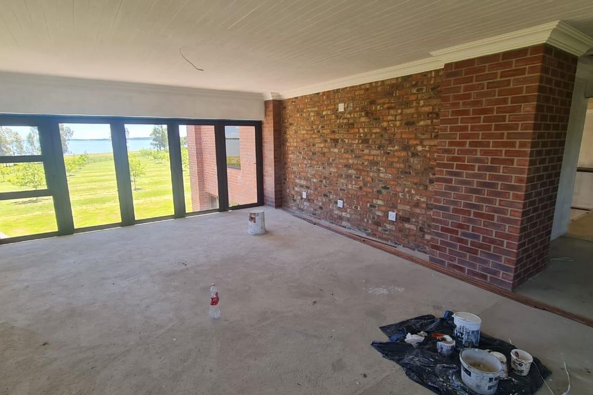 Spacious living area featuring an exposed brick wall, large folding doors with garden views, and unfinished flooring, offering a blank canvas for renovation.