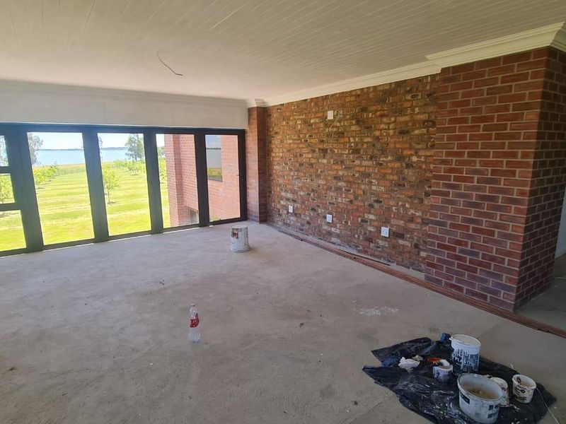 Spacious living area featuring an exposed brick wall, large folding doors with garden views, and unfinished flooring, offering a blank canvas for renovation.