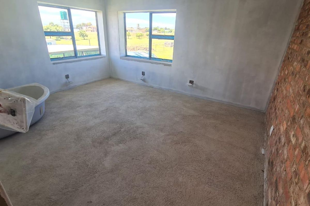 An unfinished bedroom space featuring an exposed brick wall, carpeted flooring, and a freestanding bathtub, currently undergoing renovation with exposed wiring and plaster work.