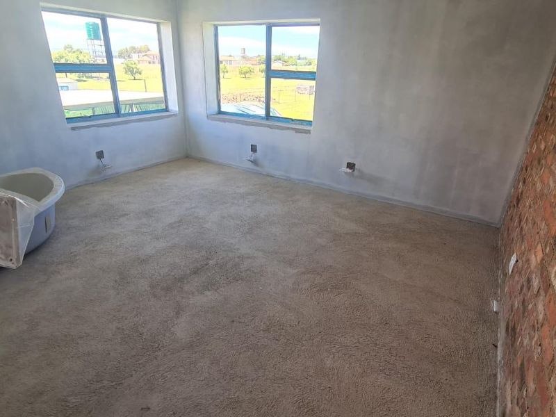 An unfinished bedroom space featuring an exposed brick wall, carpeted flooring, and a freestanding bathtub, currently undergoing renovation with exposed wiring and plaster work.