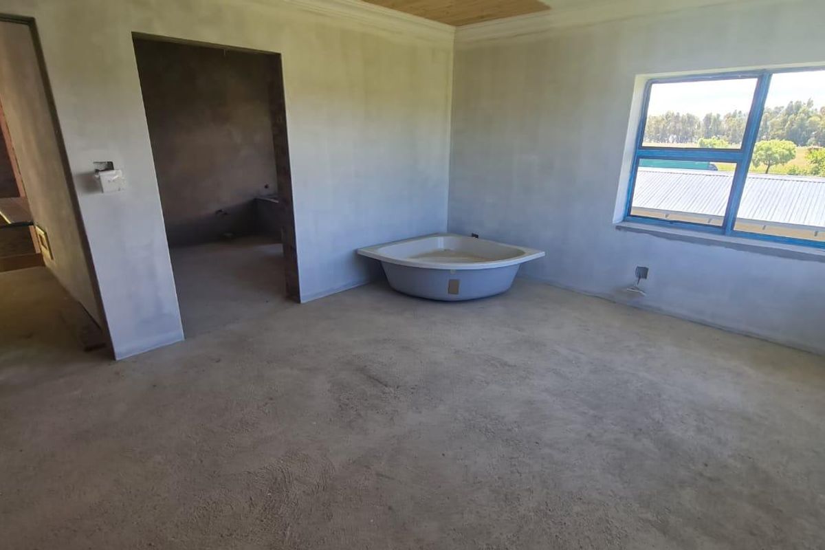 An unfinished bathroom space featuring a corner bathtub, plastered walls, and an aluminium window, currently in a shell condition awaiting final finishes.