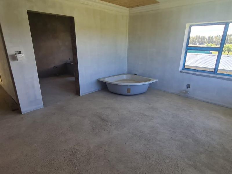 An unfinished bathroom space featuring a corner bathtub, plastered walls, and an aluminium window, currently in a shell condition awaiting final finishes.