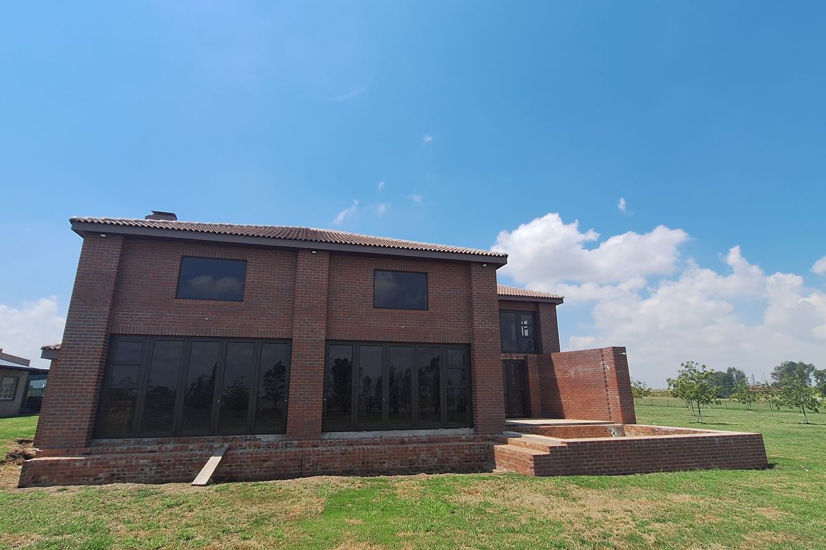 Rear view of a double-story face brick house featuring large sliding glass doors and a raised brick patio area set in a spacious garden.