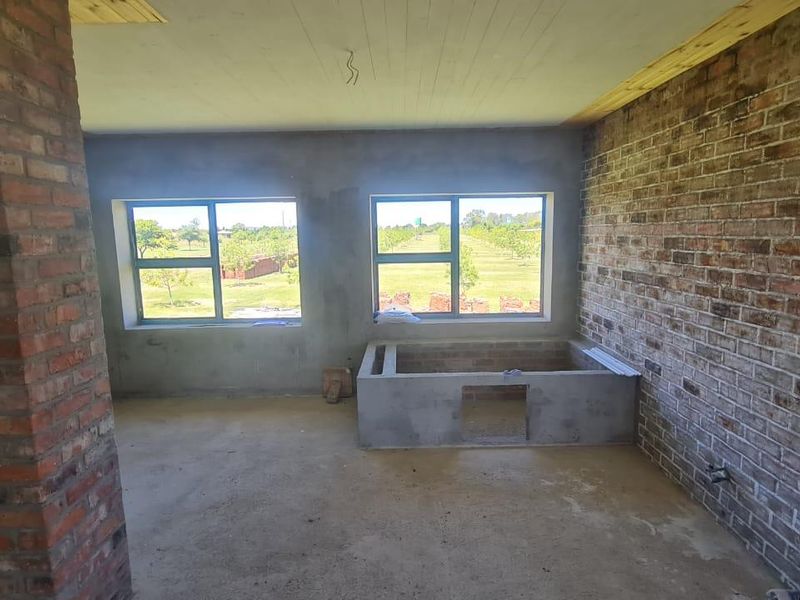 An unfinished bedroom space featuring exposed brick walls, aluminium windows, and a concrete floor, currently in a shell construction state.