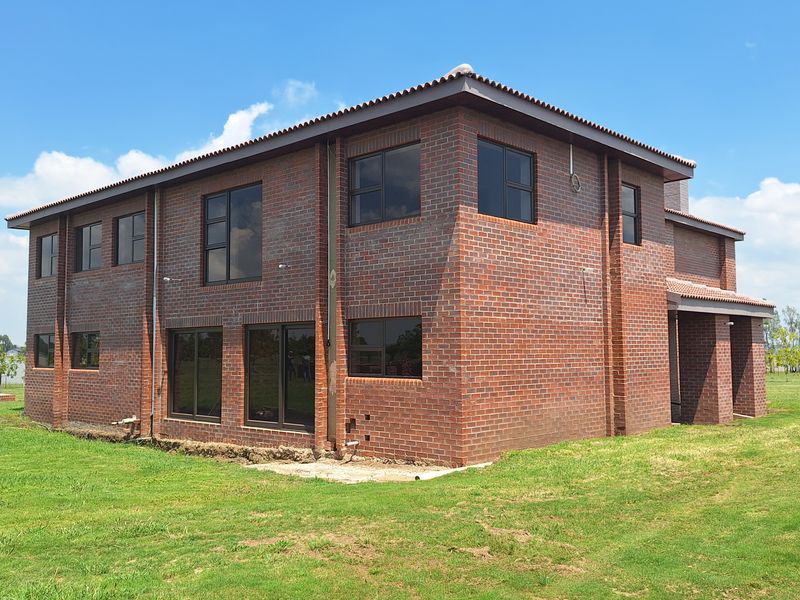 A double-storey face brick house exterior featuring aluminium window frames and sliding doors, set on a large grassed plot.
