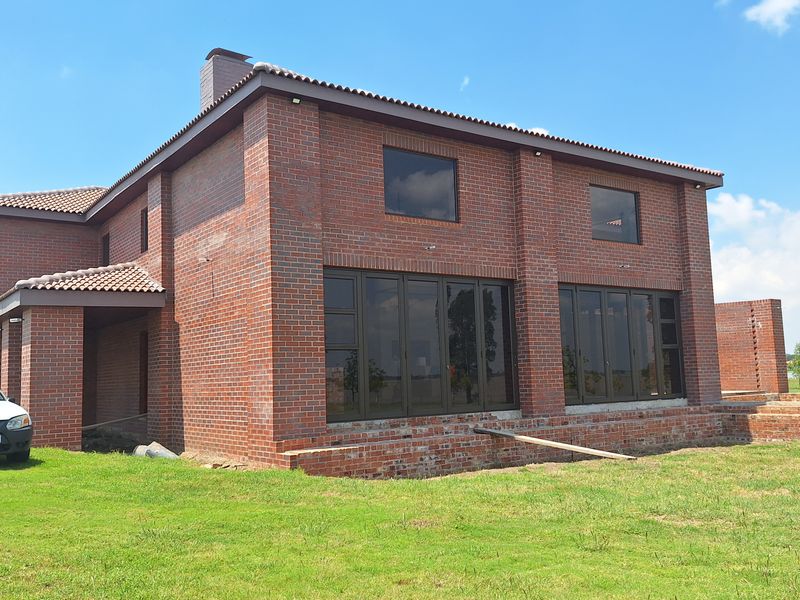 Rear view of a double-story face brick house featuring large aluminium folding doors and a tiled roof, set on a spacious lawn.