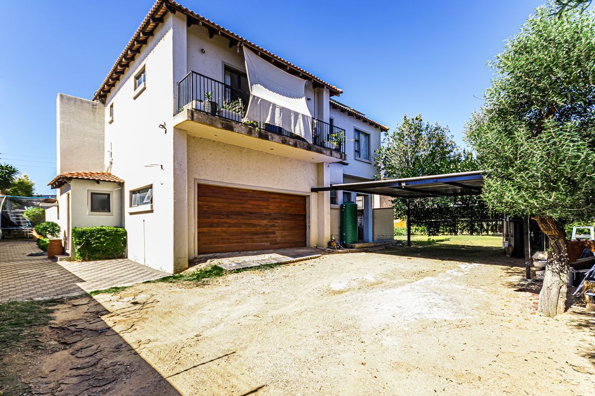 Rear view of the property featuring a double garage, a covered carport, and an upper-level balcony with metal railings.