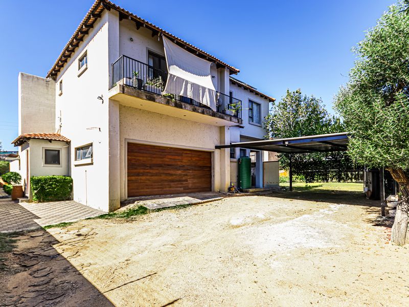Rear view of the property featuring a double garage, a covered carport, and an upper-level balcony with metal railings.
