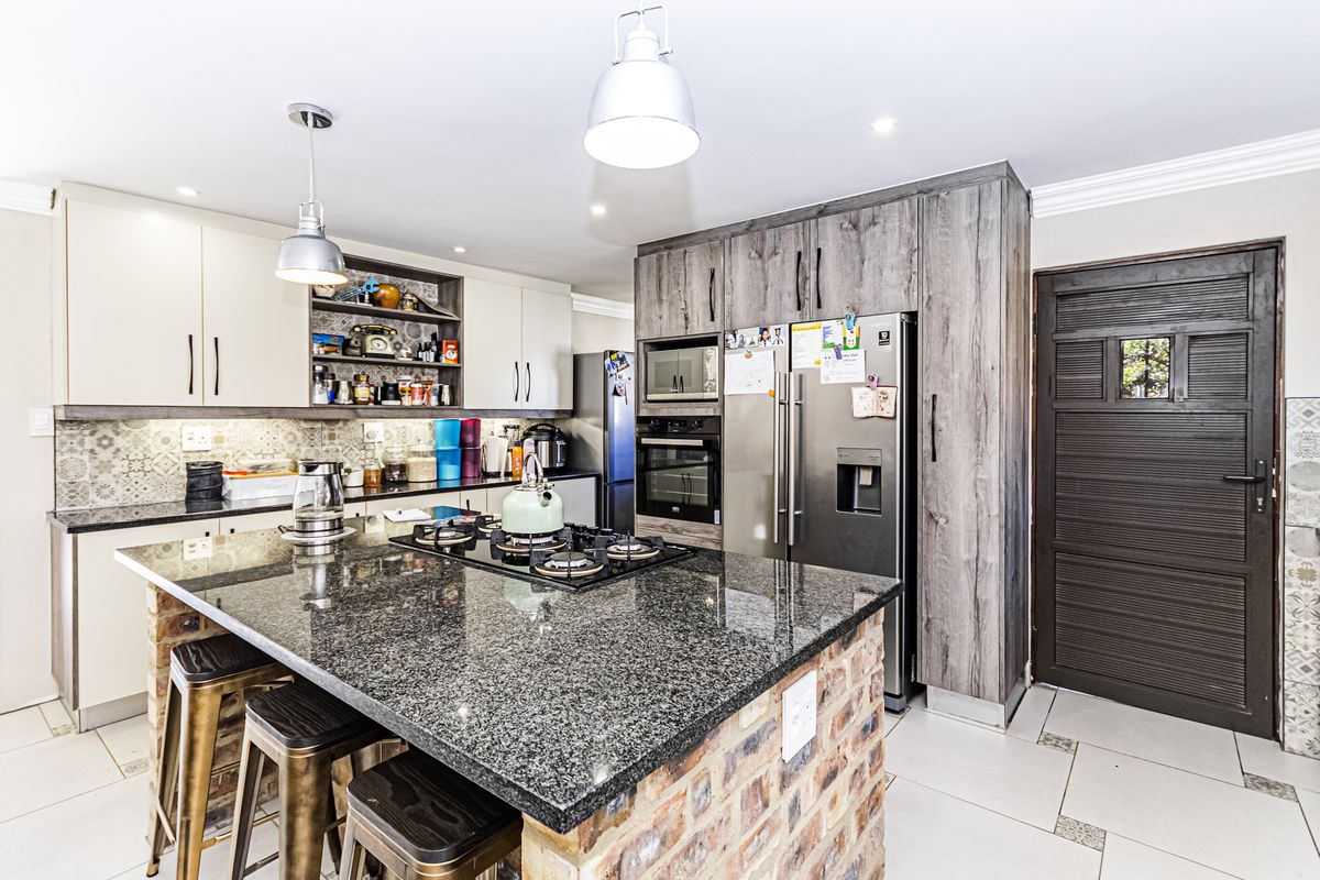 Modern kitchen featuring a granite-topped island with exposed brick base, built-in appliances, patterned backsplash, and ample cabinetry.
