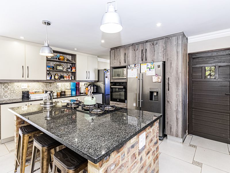 Modern kitchen featuring a granite-topped island with exposed brick base, built-in appliances, patterned backsplash, and ample cabinetry.