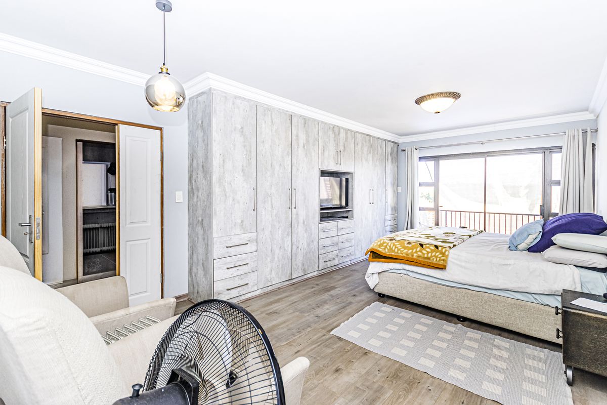 Spacious bedroom featuring extensive built-in cupboards, laminate flooring, and a sliding glass door providing access to an outdoor area.