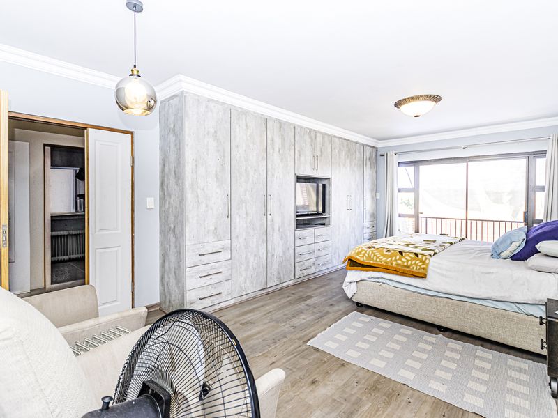 Spacious bedroom featuring extensive built-in cupboards, laminate flooring, and a sliding glass door providing access to an outdoor area.