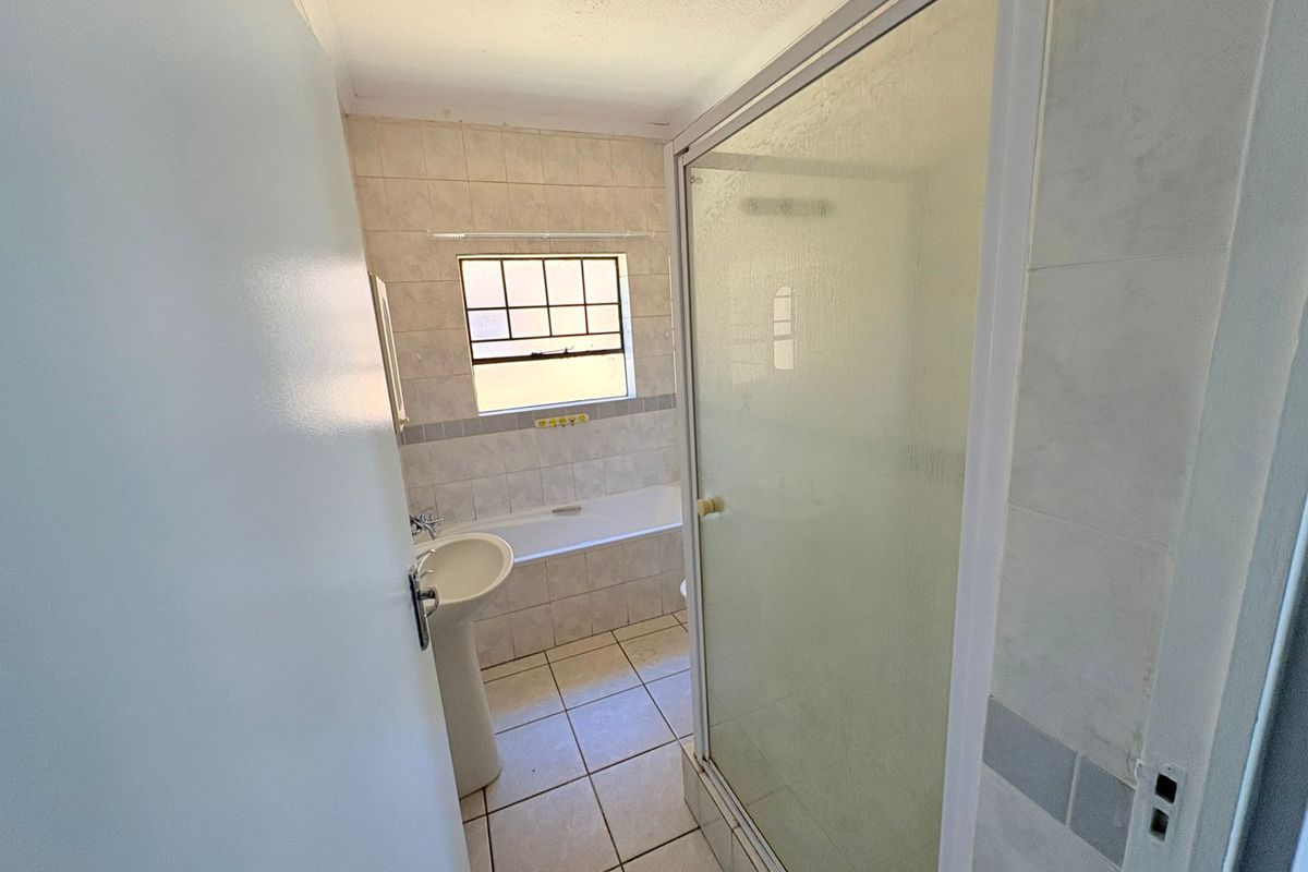 A functional bathroom featuring a pedestal basin, a built-in bathtub, and a separate glass-enclosed shower with tiled walls and flooring.