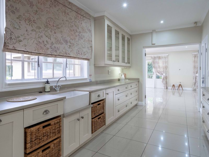 A bright, modern kitchen featuring shaker-style cabinetry, a classic farmhouse sink, stone countertops, and polished tile flooring with seamless flow to the adjacent living area.