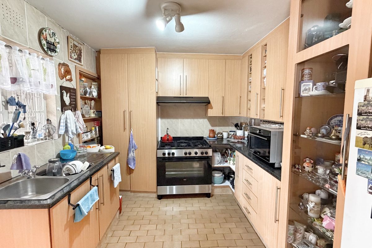 A functional kitchen featuring light wood cabinetry, a gas stove with extractor fan, double sink, and tiled flooring with ample built-in storage.