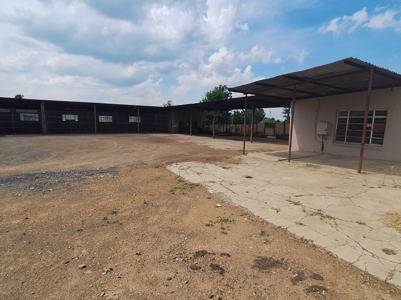 Expansive outdoor area featuring a large covered structure with steel supports, concrete flooring, and security-barred windows, suitable for storage or workshop use.