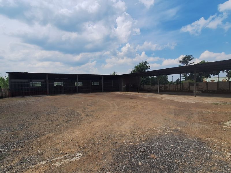 Large open-sided industrial-style garage or storage structure with a gravel yard and metal security enclosures.