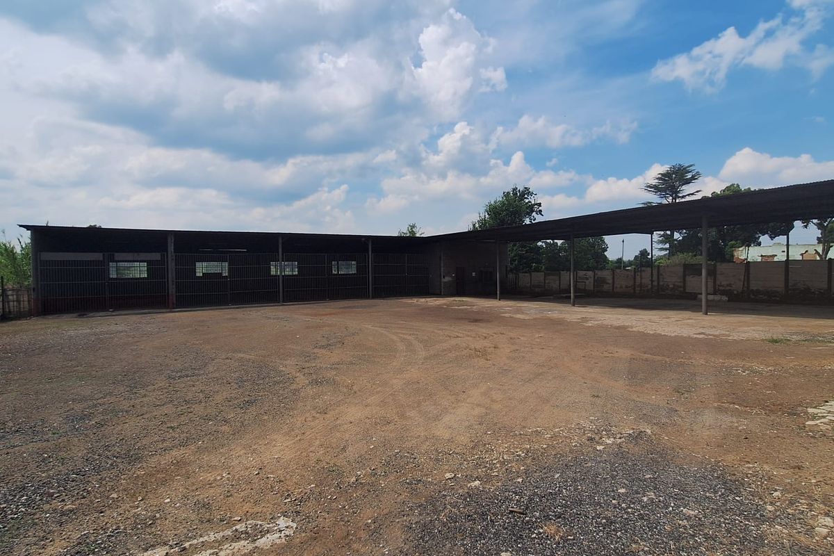 Large open-sided industrial-style garage or storage structure with a gravel yard and metal security enclosures.