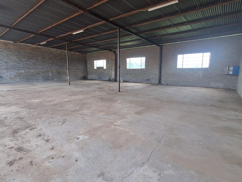A large, open-plan utility or workshop space featuring exposed brick walls, a corrugated metal roof, and a concrete floor with visible cracking.