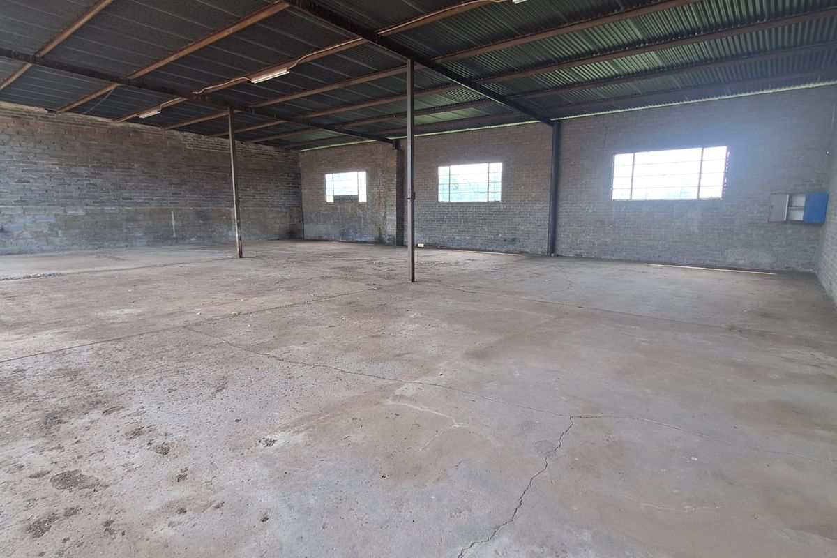A large, open-plan utility or workshop space featuring exposed brick walls, a corrugated metal roof, and a concrete floor with visible cracking.