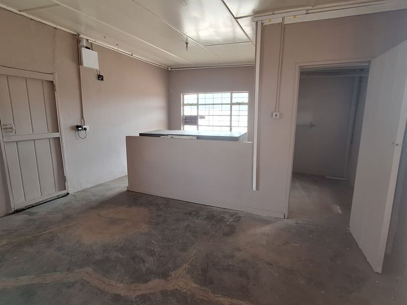An empty utility or storage space featuring a concrete floor, tiled ceiling, and access to an adjacent room.