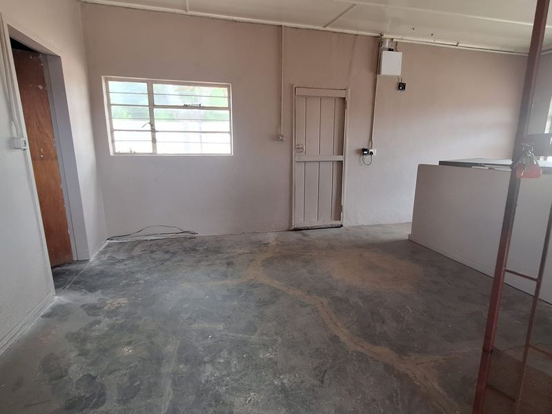 An empty, unfinished living area featuring concrete flooring, exposed electrical conduit, and a simple timber door, offering a blank canvas for renovation.