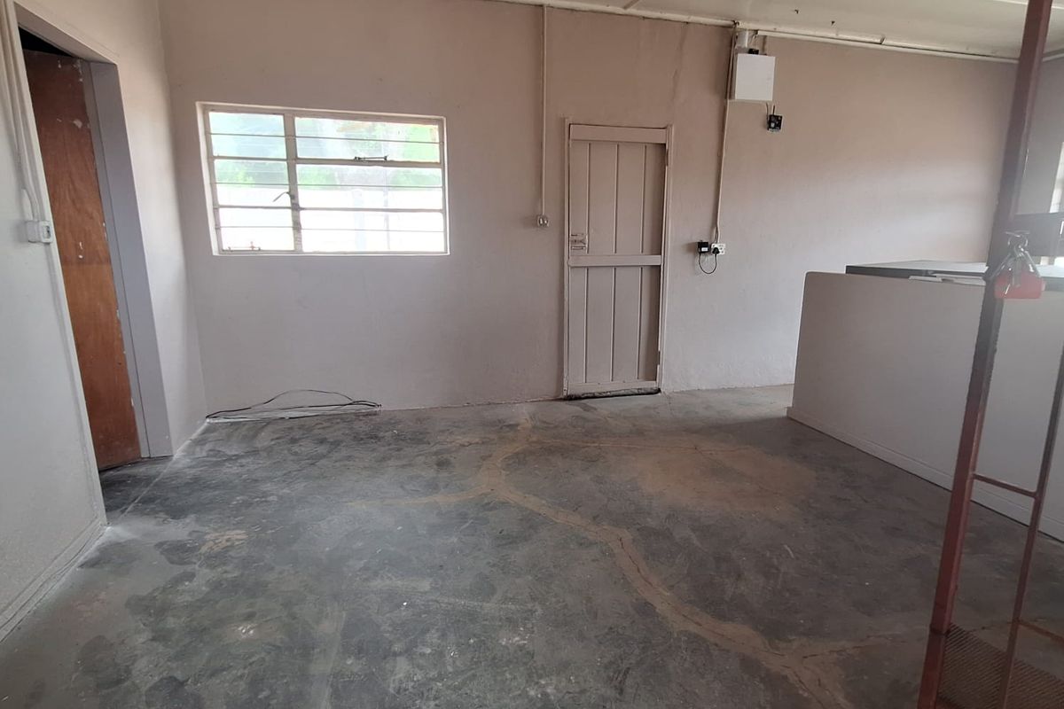 An empty, unfinished living area featuring concrete flooring, exposed electrical conduit, and a simple timber door, offering a blank canvas for renovation.