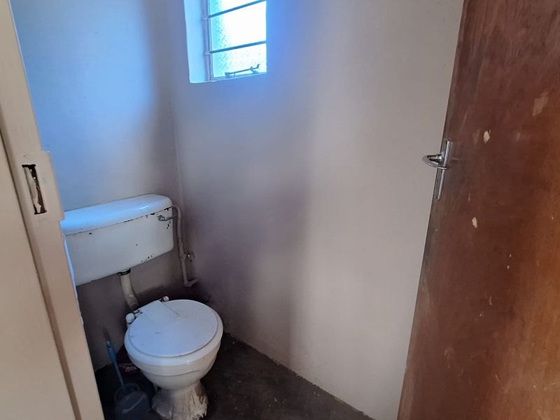 A small, dated bathroom featuring a standard toilet and a small obscured glass window, requiring cosmetic updates and repairs.
