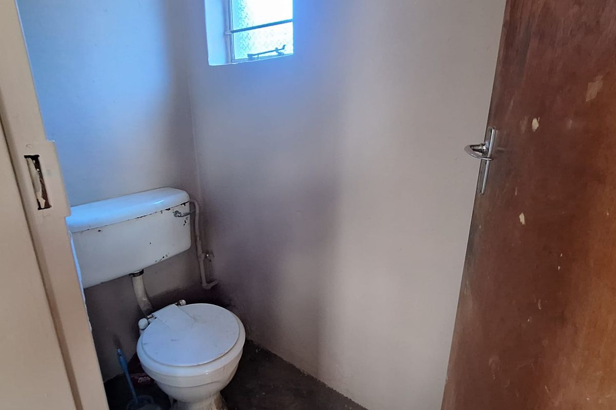 A small, dated bathroom featuring a standard toilet and a small obscured glass window, requiring cosmetic updates and repairs.