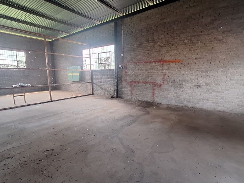 An expansive, unfinished utility space featuring exposed brick walls, a corrugated metal roof, and concrete flooring, suitable for workshop or storage conversion.