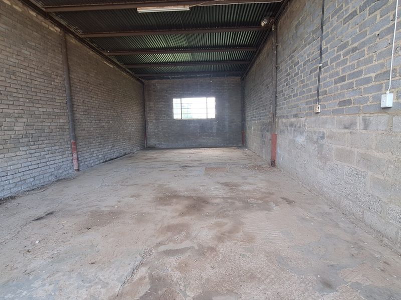 A spacious, unfinished garage or utility space featuring exposed brick walls, a corrugated metal roof, and a concrete floor.