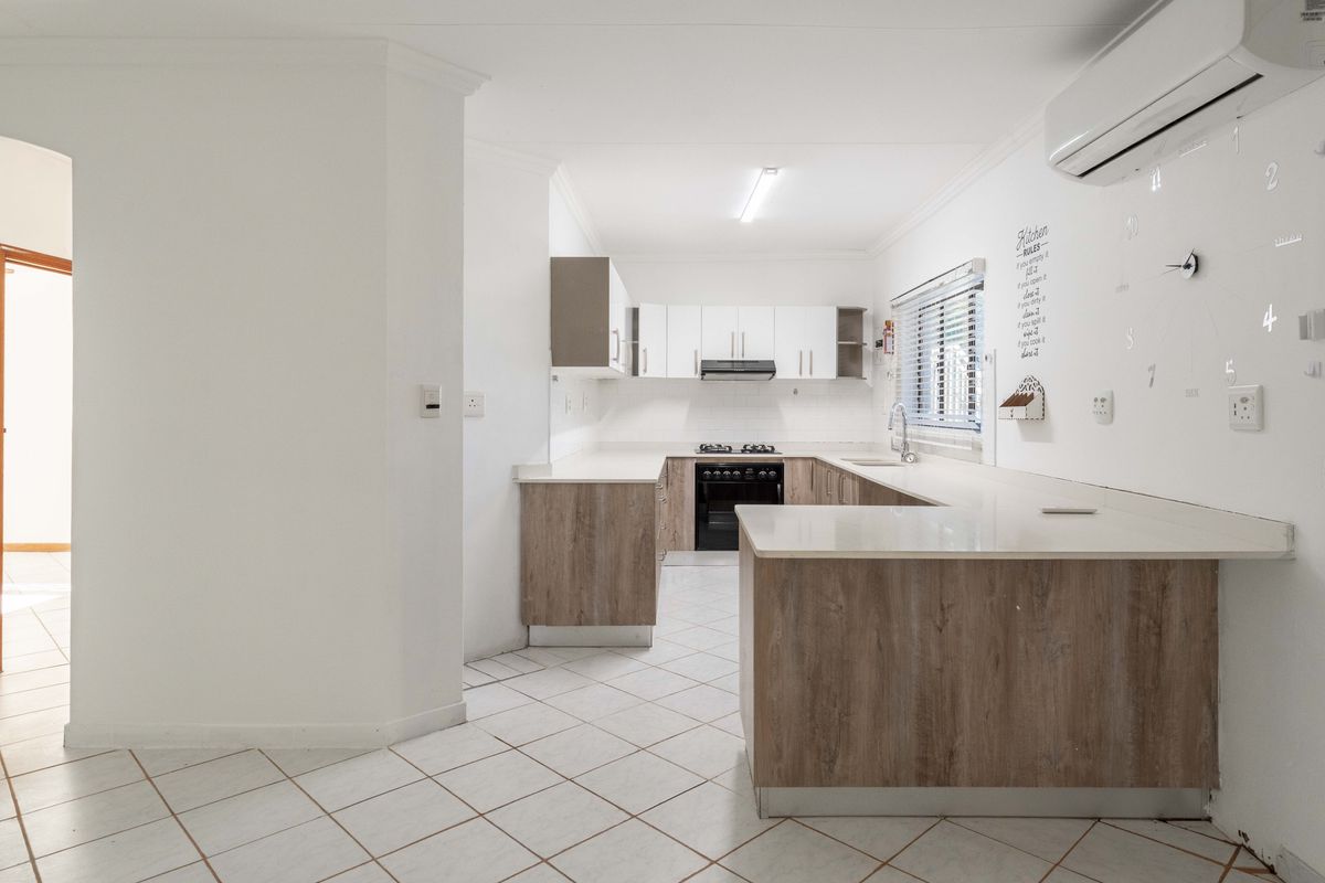 A clean, U-shaped kitchen featuring wood-look cabinetry, white stone countertops, a built-in oven with extractor fan, and tiled flooring.