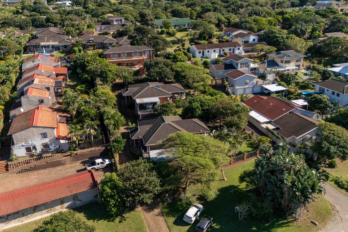 An aerial view of a residential townhouse complex featuring tiled roofs, established gardens, and surrounding neighborhood infrastructure.