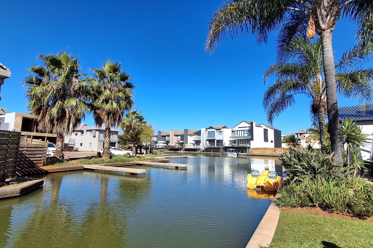 A scenic view of a residential waterway featuring private jetties, manicured gardens, and established palm trees within a modern estate setting.