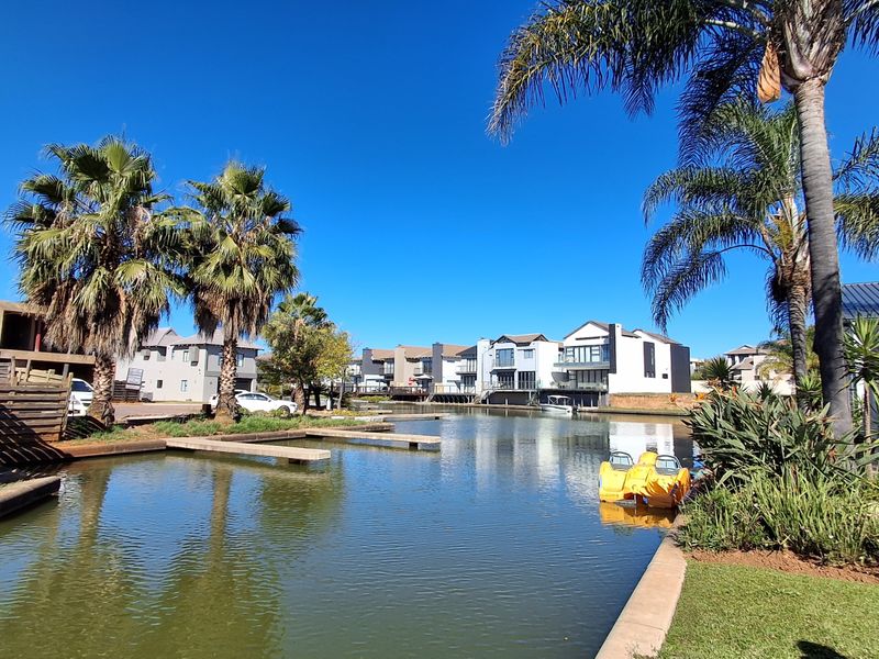 A scenic view of a residential waterway featuring private jetties, manicured gardens, and established palm trees within a modern estate setting.