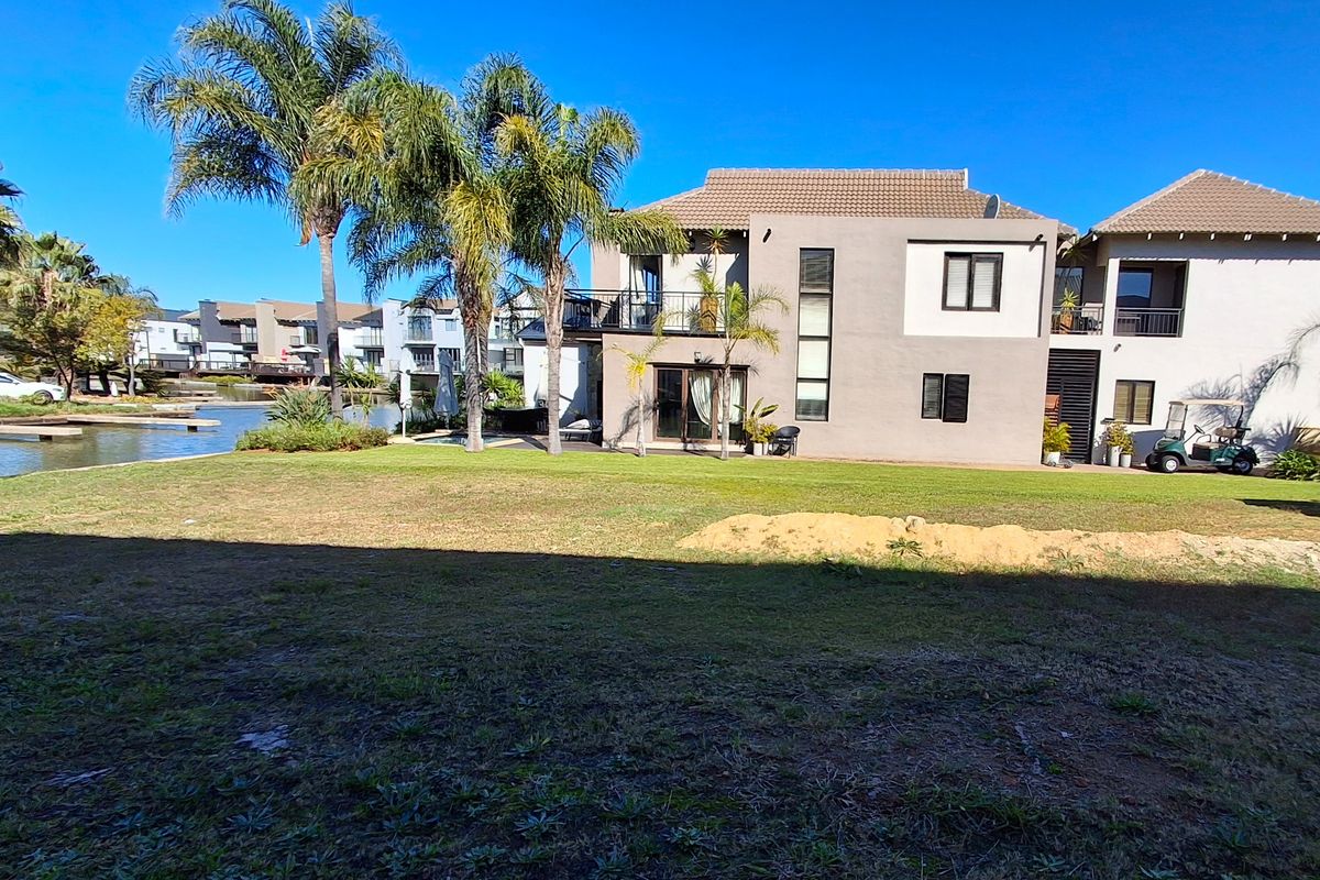 Rear view of a multi-story residential property featuring a balcony, landscaped garden, and direct waterfront access in a well-maintained estate setting.