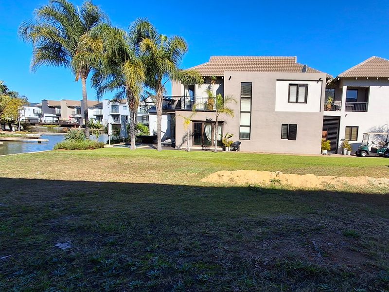 Rear view of a multi-story residential property featuring a balcony, landscaped garden, and direct waterfront access in a well-maintained estate setting.